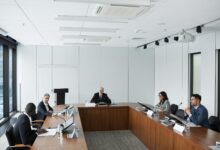 Professional conference room with people in business attire seated around a large table during a formal meeting