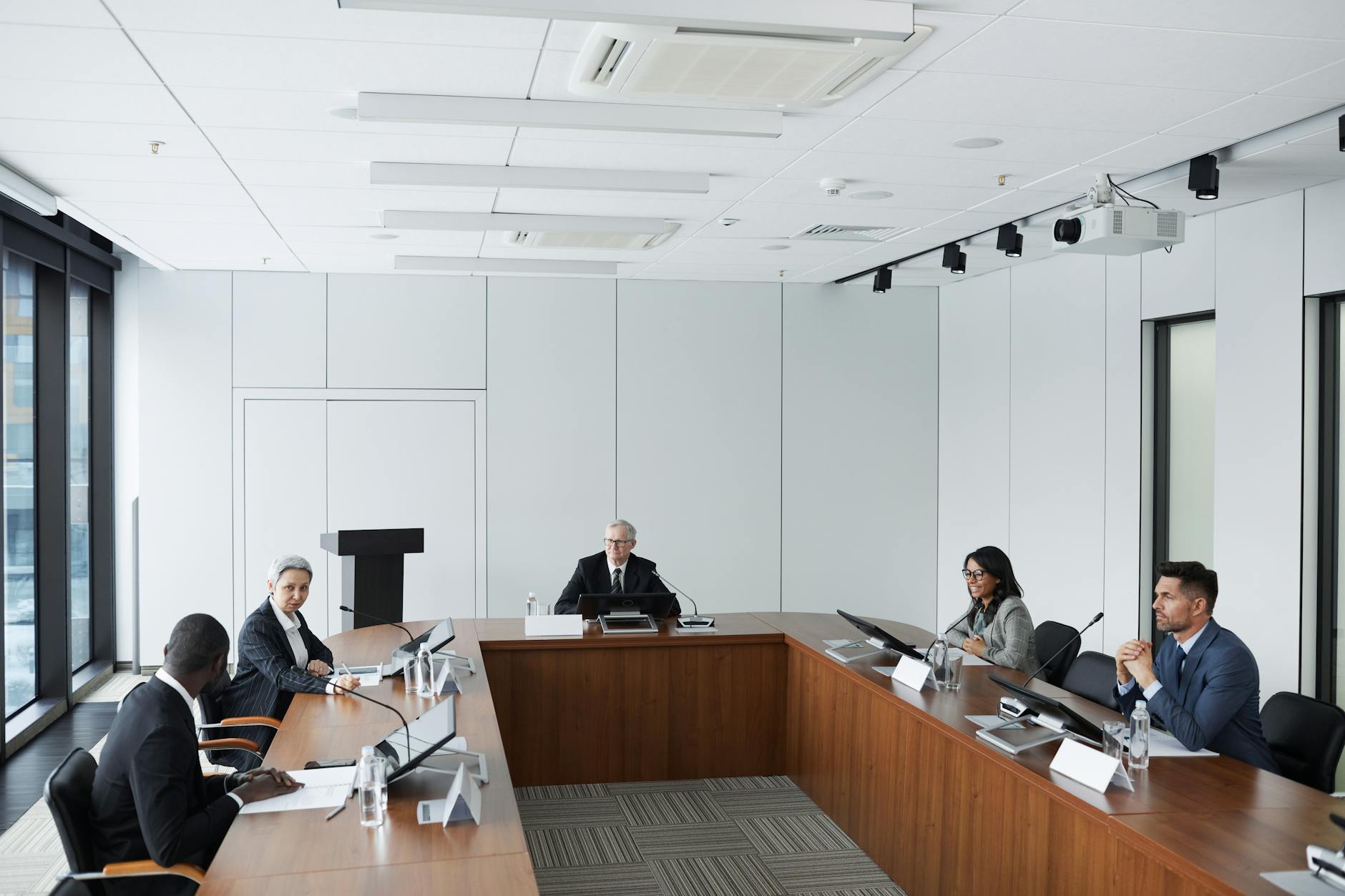 Professional conference room with people in business attire seated around a large table during a formal meeting