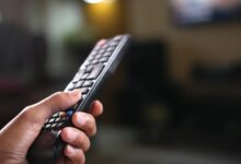 Person holding television remote control with streaming service logos on screen