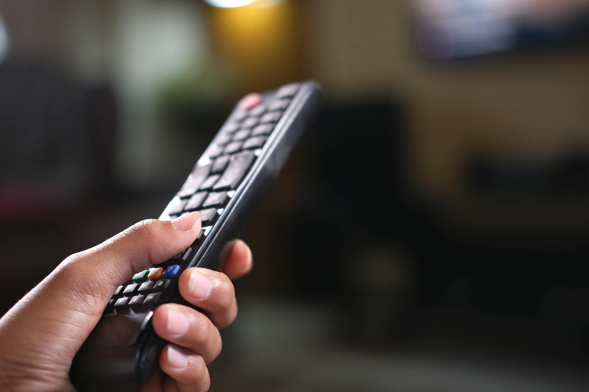 Person holding television remote control with streaming service logos on screen