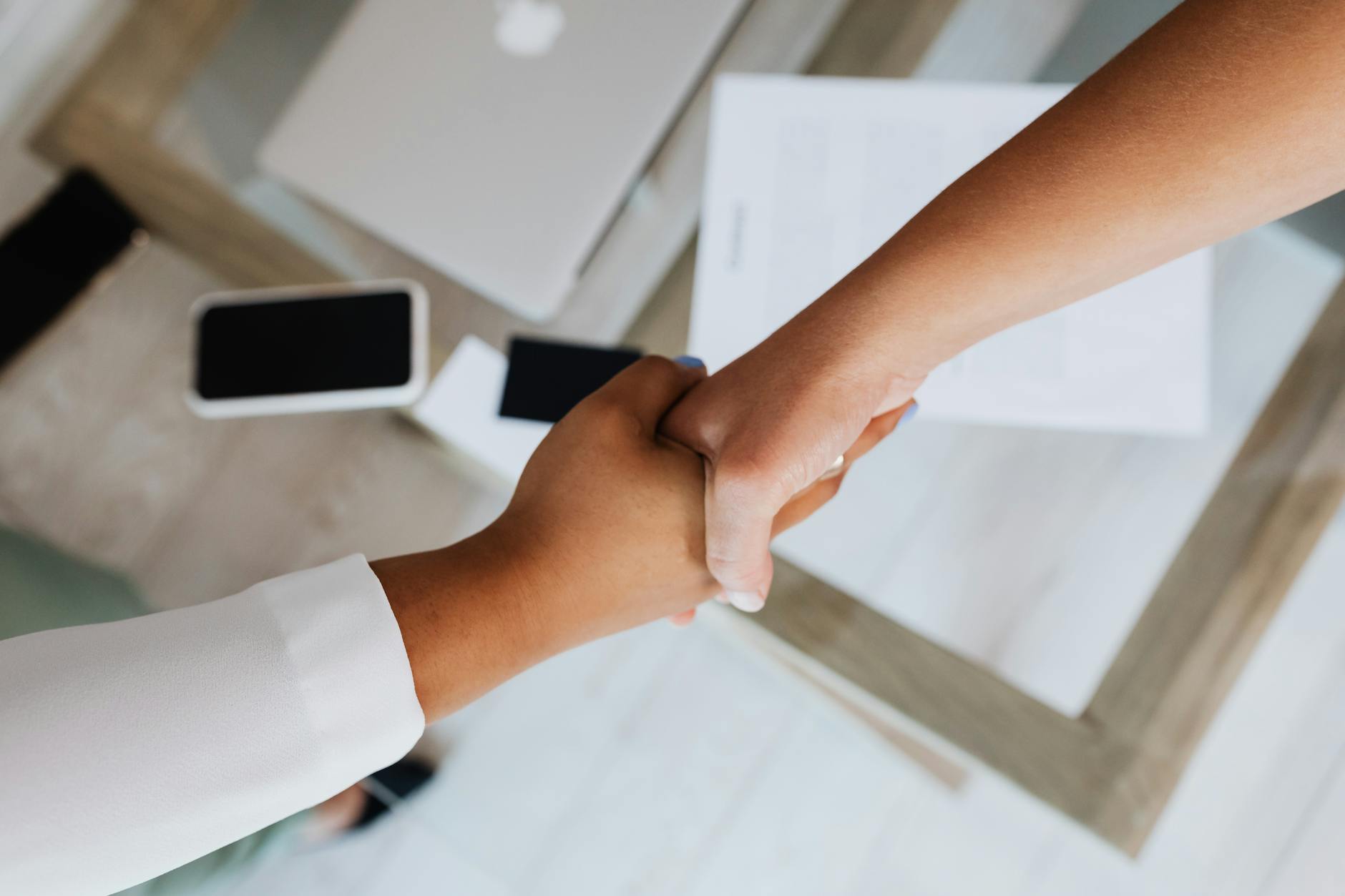 Two people shaking hands across desk in professional business setting