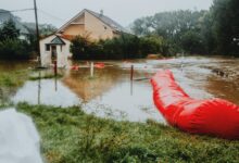 Residential neighborhood streets submerged in floodwater with homes visible in background