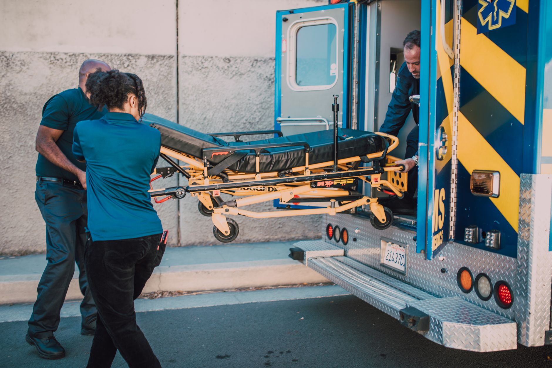 Paramedics loading a patient onto a stretcher beside an ambulance