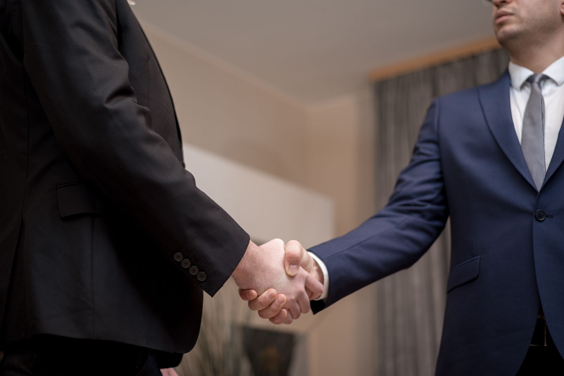 Two business professionals shaking hands across a table during an acquisition meeting