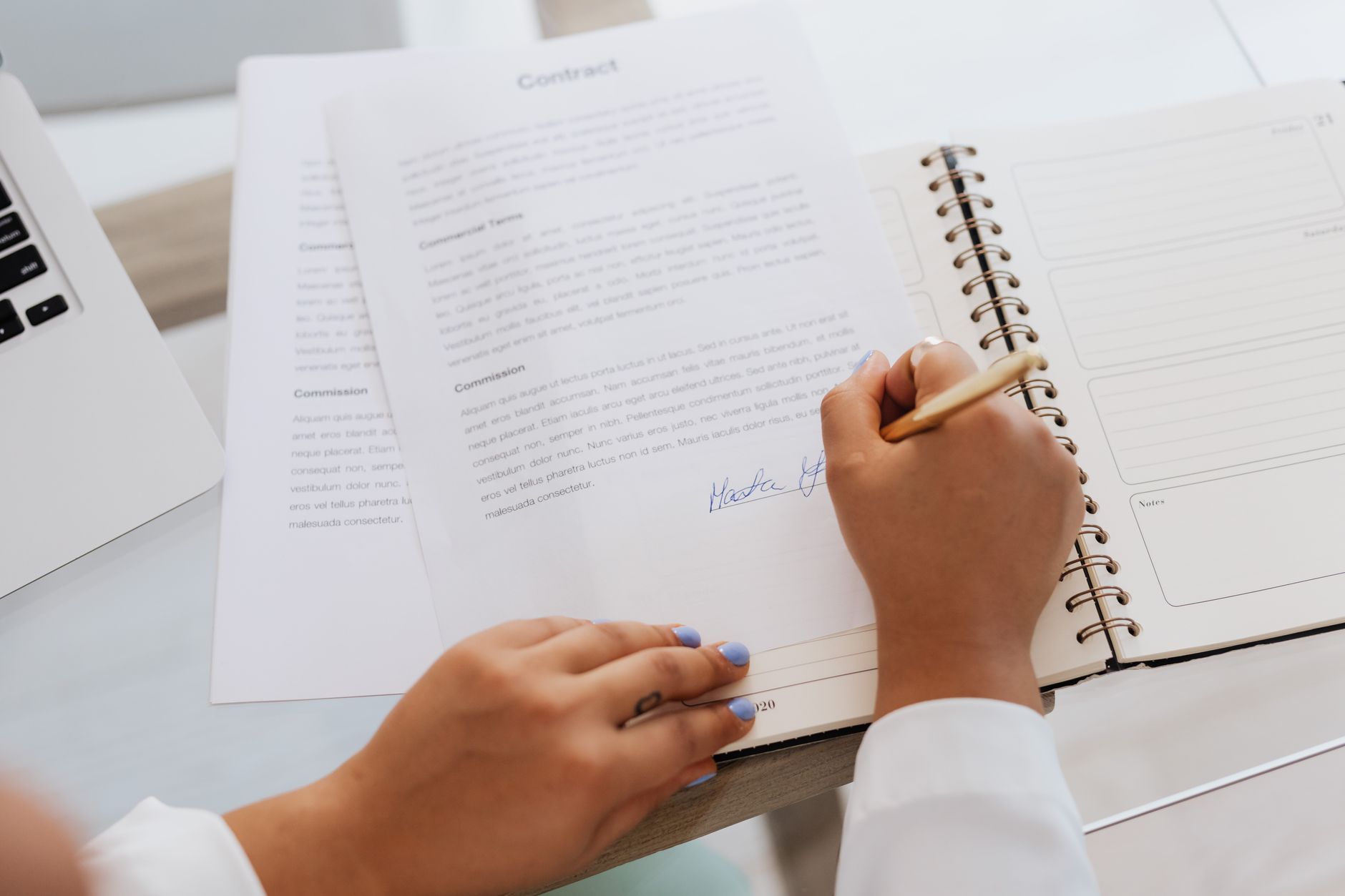 Two people reviewing and signing a business acquisition contract at a desk