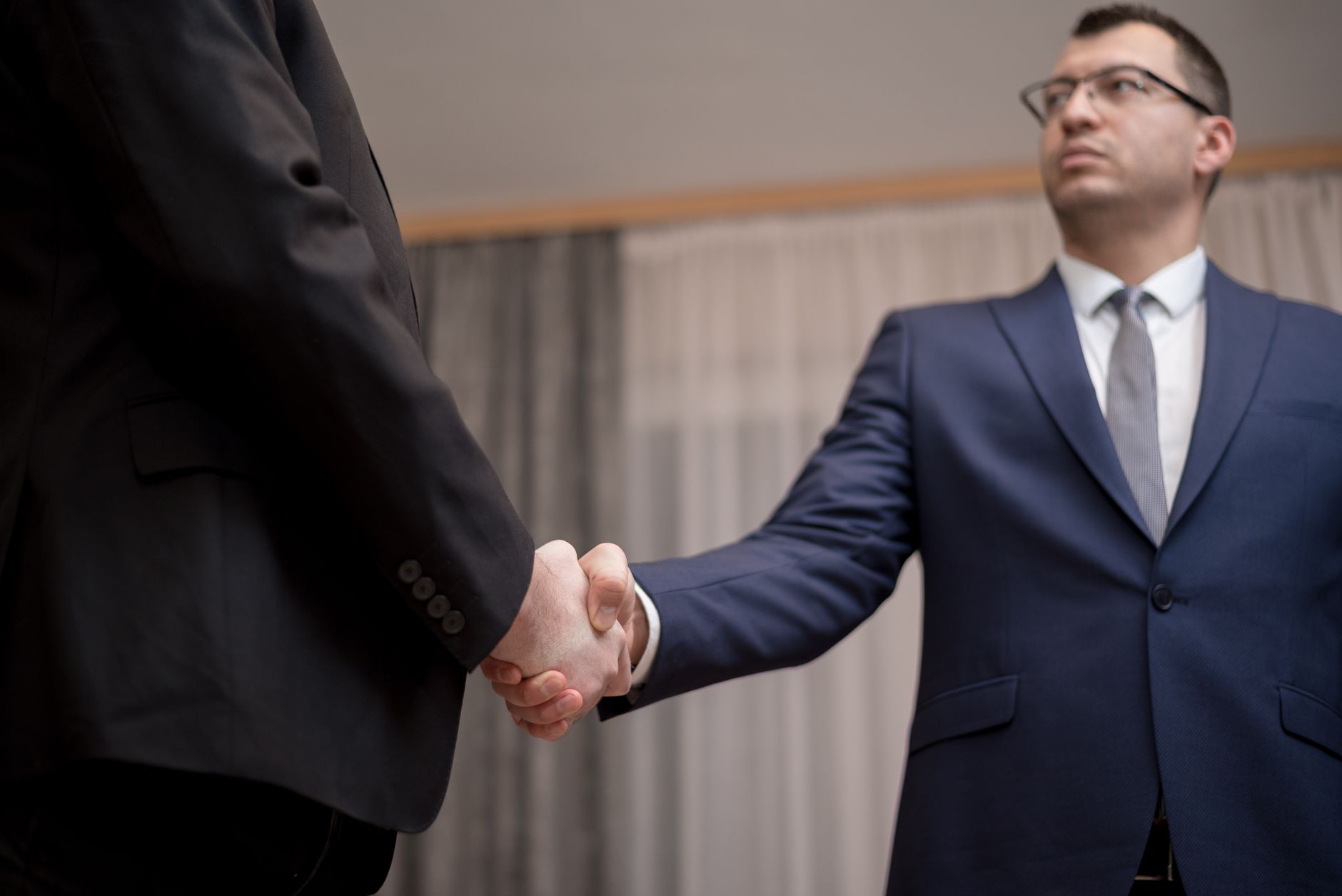 Two professionals shaking hands across a desk during a business acquisition meeting