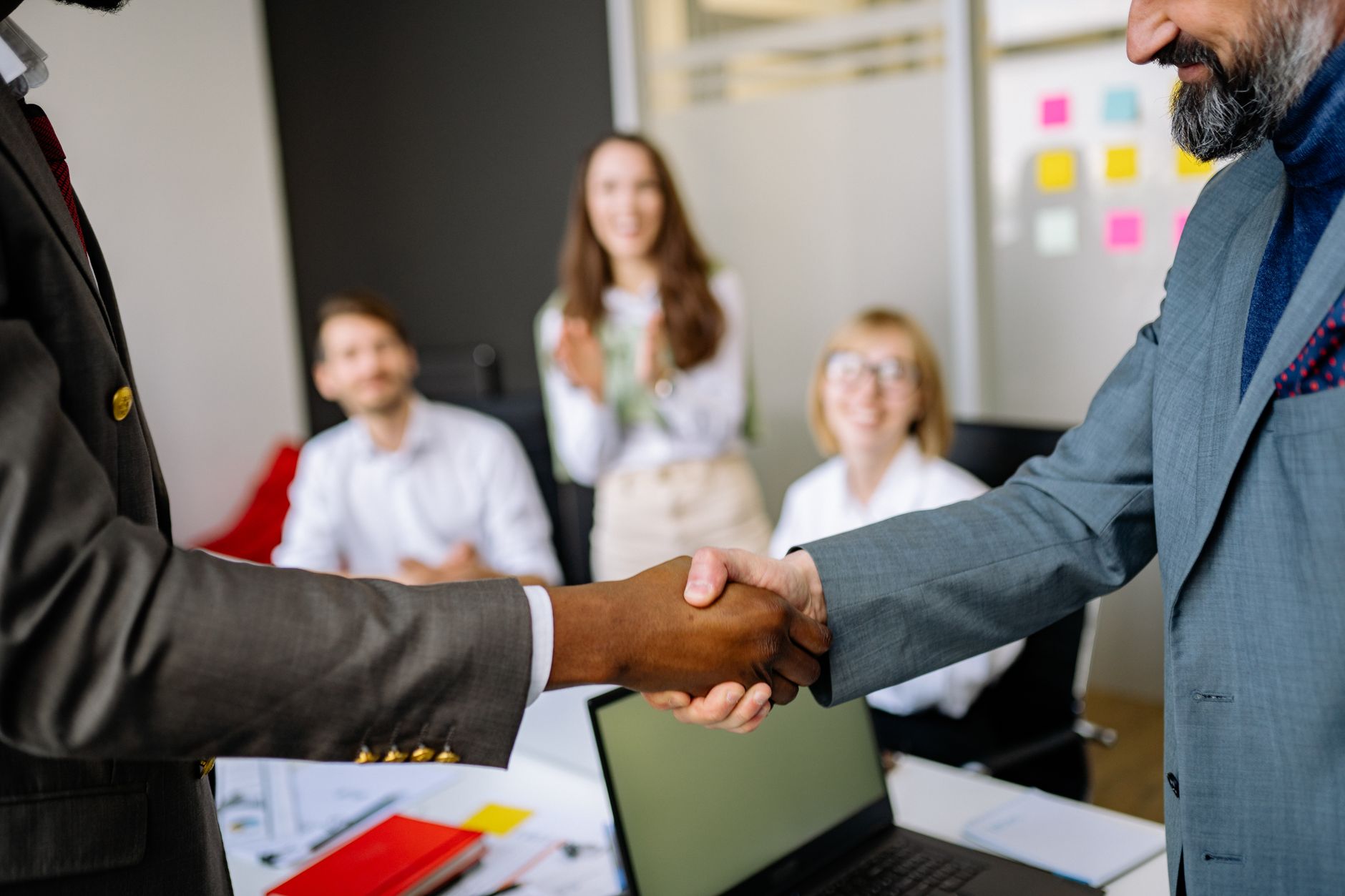 Two professionals shaking hands across a desk during a business transaction