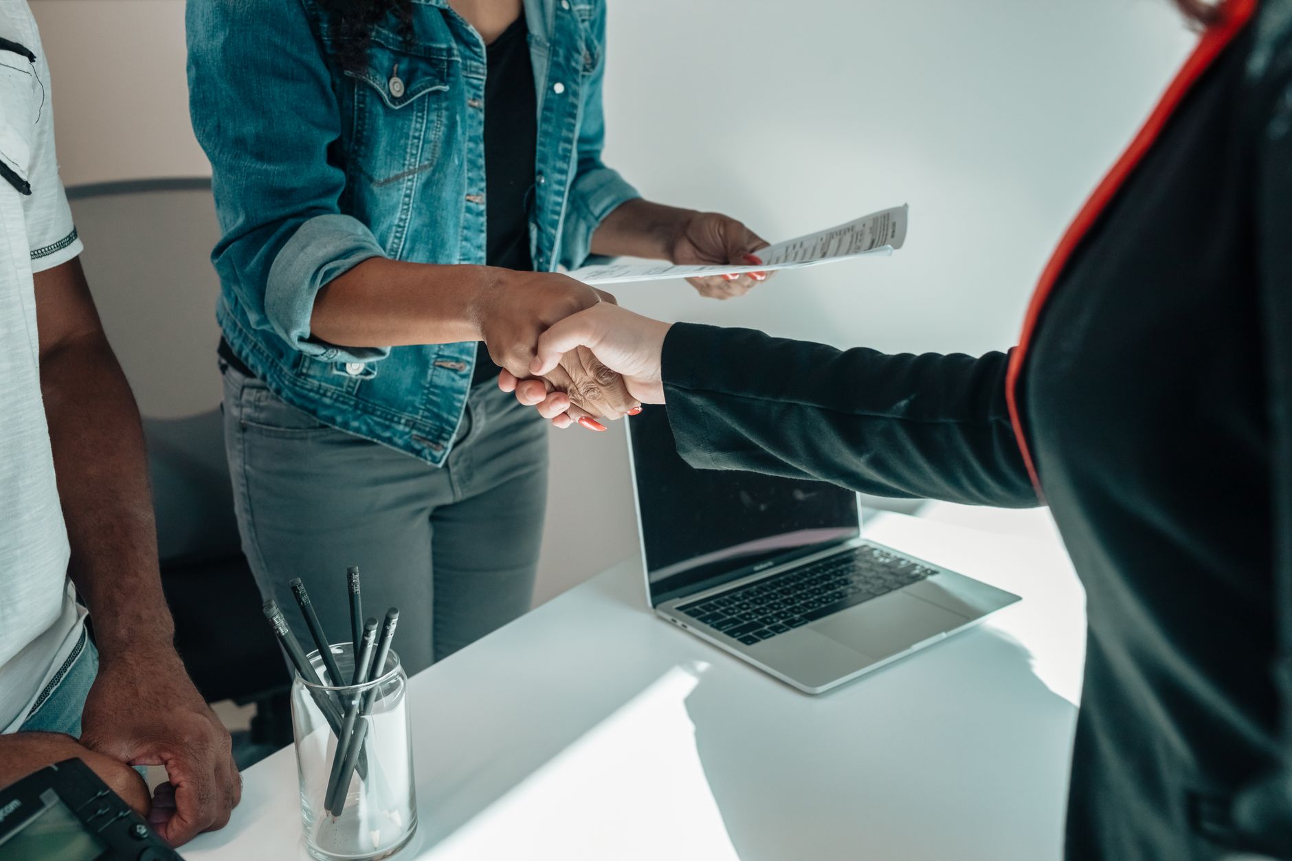 Two business professionals shaking hands across a desk during a meeting
