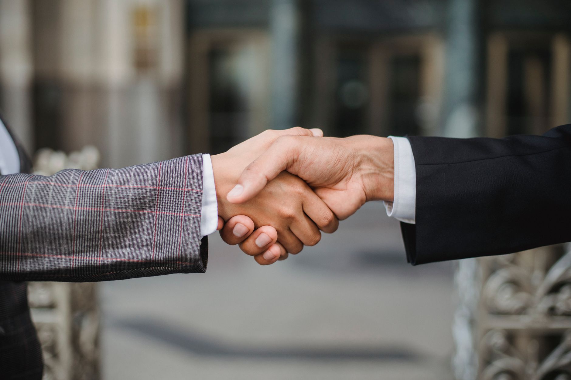 Two professionals shaking hands across a conference table during a business acquisition meeting