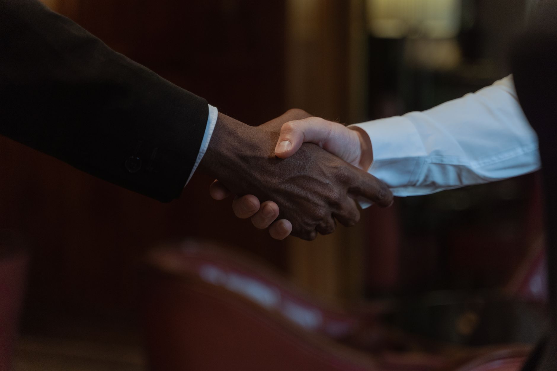 Two business professionals shaking hands across a desk during a meeting